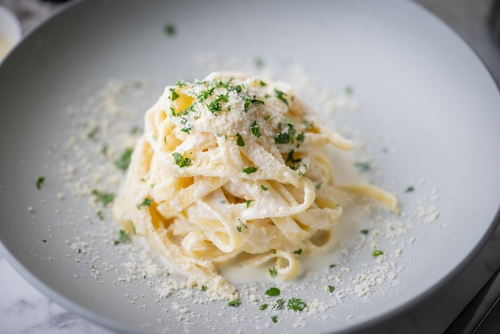 Nesta imagem, há um macarrão fettuccine com molho branco em prato branco