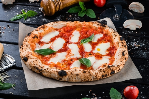 Na imagem, há uma pizza napolitana com molho de tomate, queijo e manjericão