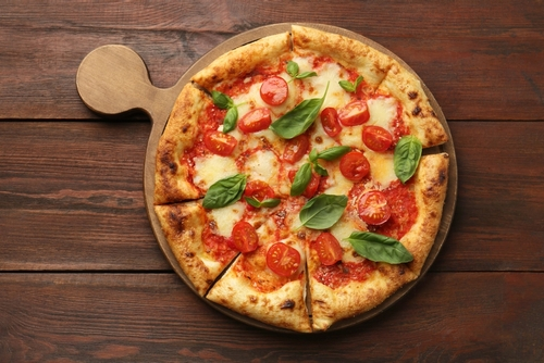 Na imagem, há pizza marguerita com tomate e manjericão em cima de tábua para assar pizza