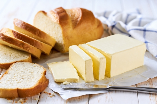 Nesta imagem há uma manteiga em formato tablete retangular com fatias de pão sobre a mesa.