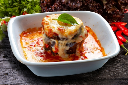 Na imagem, há uma lasanha de berinjela com molho de tomate e queijo derretido