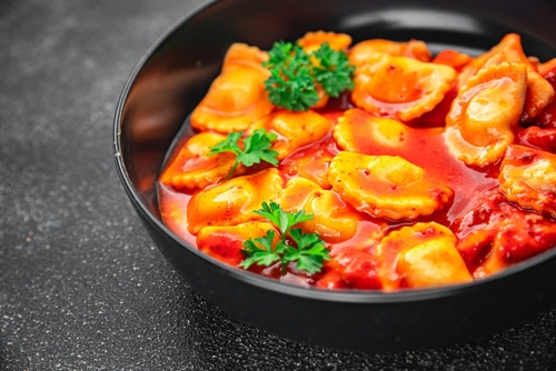 Na imagem, há um prato fundo com massa agnolotti mergulhada em molho de tomate