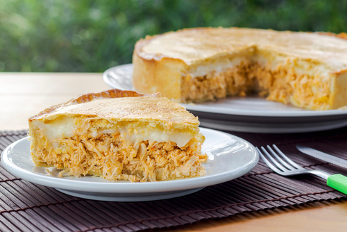 Na imagem, há uma torta de frango com requeijão com destaque em uma fatia cortada