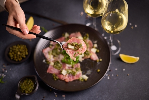 Na imagem, há uma panela com comida italiana carpaccio, com destaque para pedaço de carpaccio em uma colher